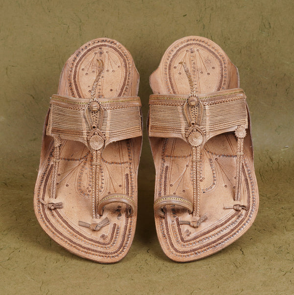 Pair of traditional leather sandals with intricate designs on a textured green background